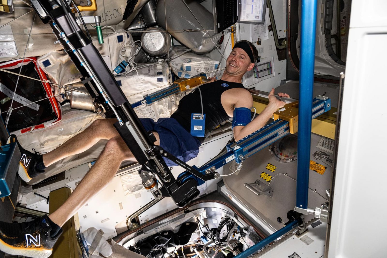 O astronauta da NASA Nick Hague se exercita no Advanced Resistive Exercise Device da Estação Espacial Internacional enquanto usa o colete e a faixa de cabeça Bio-Monitor 
