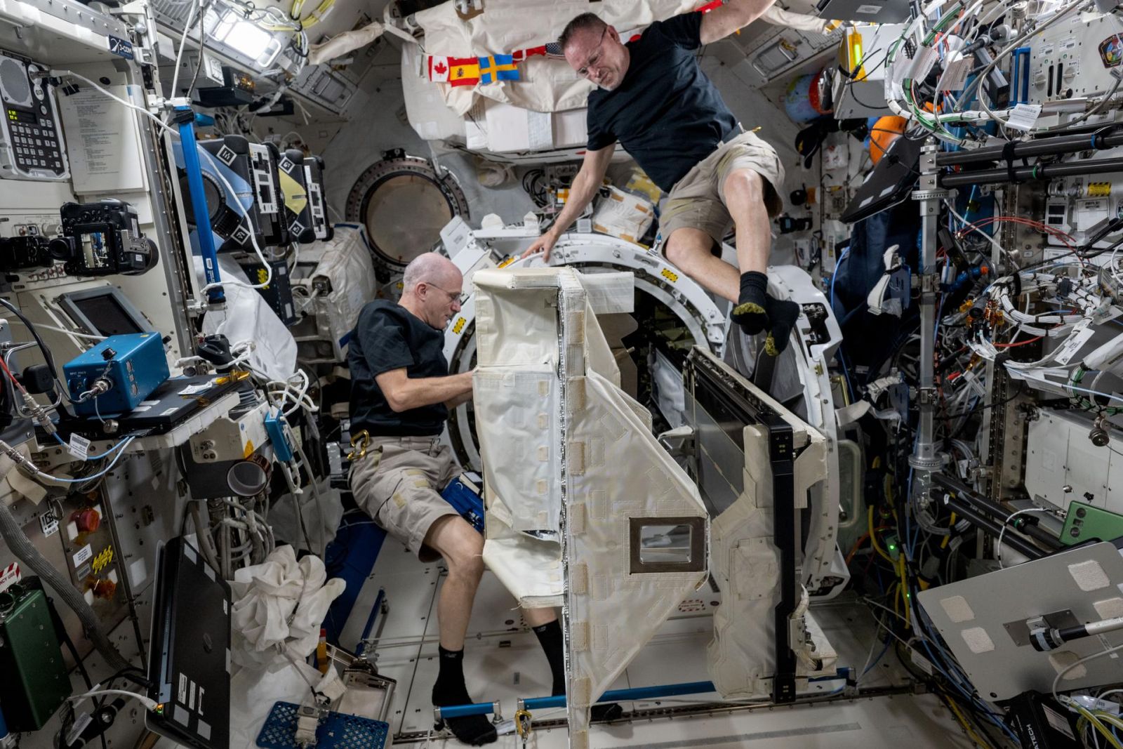 Os astronautas da NASA Don Pettit e Butch Wilmore removem um pequeno implantador de satélite de uma câmara de descompressão